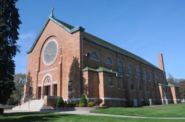 Exterior of Holy Name Church. A brick building with green roof. There is a large circular window at the front of the church.
